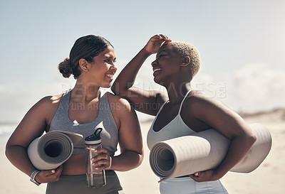 Buy stock photo Shot of two young women holding their yoga mats while  on the beach