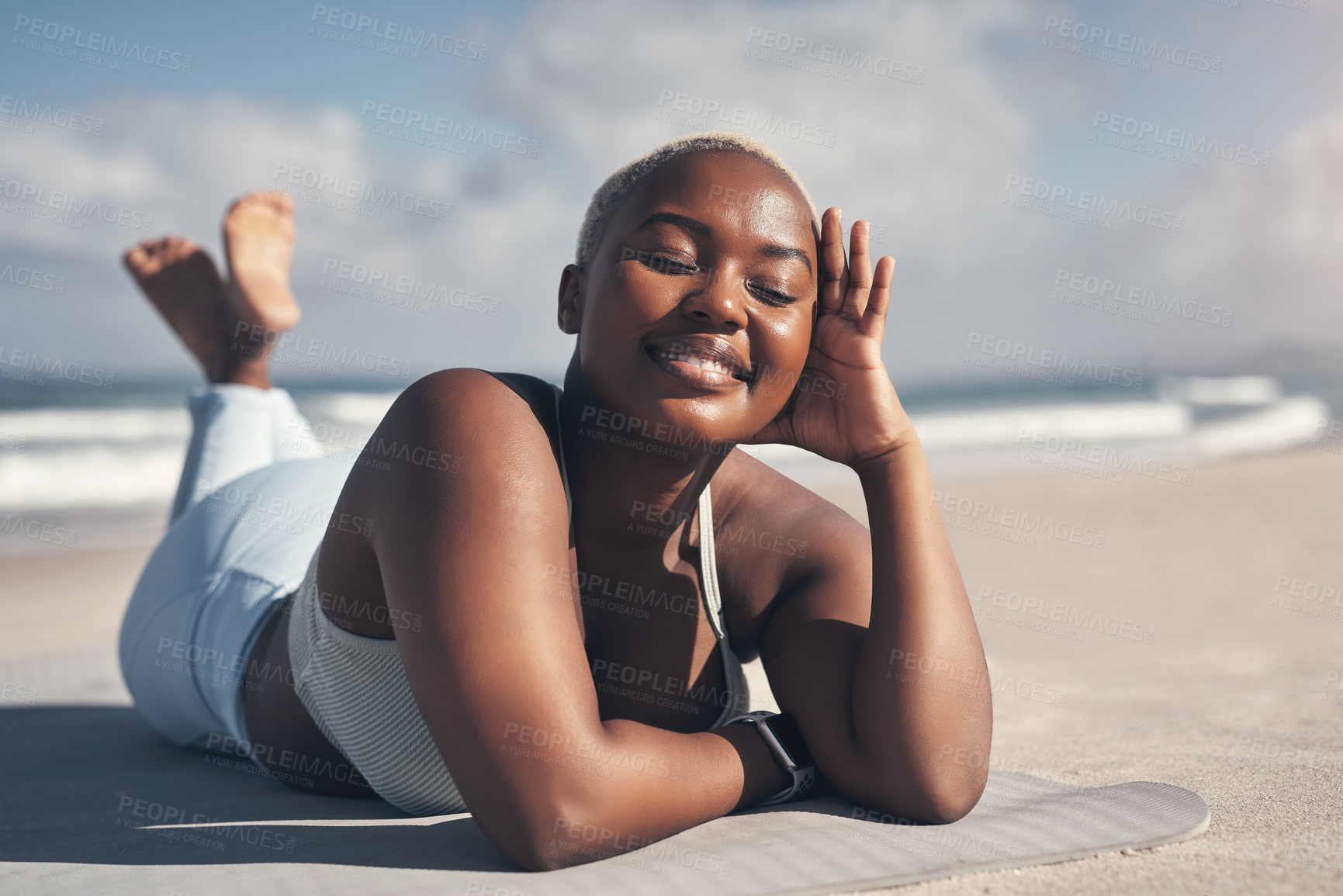 Buy stock photo Shot of a sporty young woman lying on her yoga mat at the beach