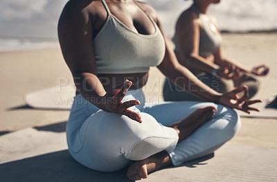 Buy stock photo Shot of two young women meditating during their yoga routine on the beach