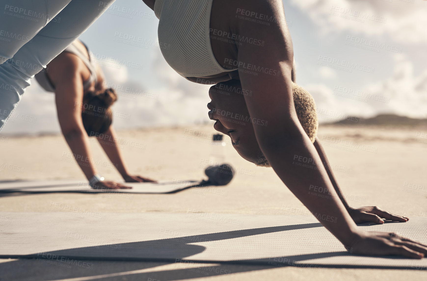 Buy stock photo Shot of two young women practicing yoga on the beach