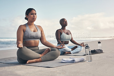 Buy stock photo Shot of two young women meditating during their yoga routine on the beach