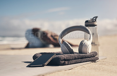 Buy stock photo Shot of a cellphone, headphones, towel and water bottle on the beach