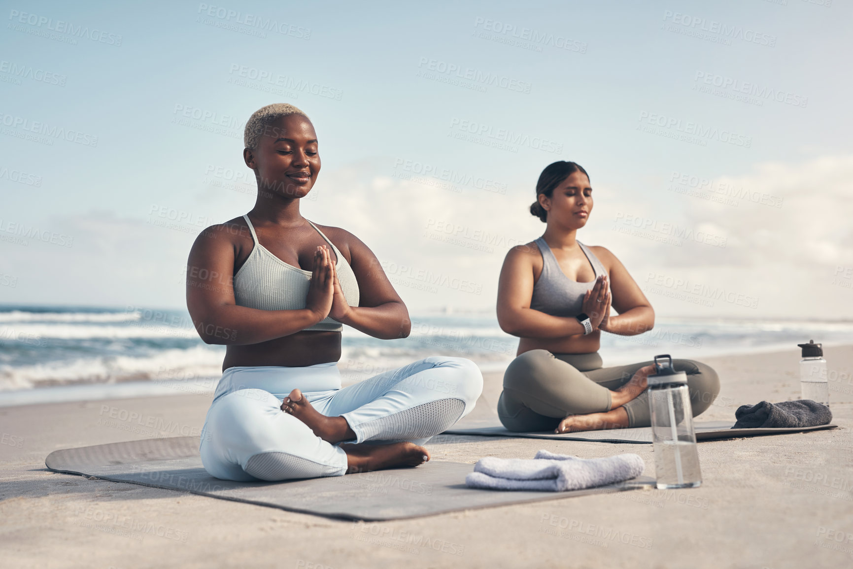 Buy stock photo Shot of two young women meditating during their yoga routine on the beach