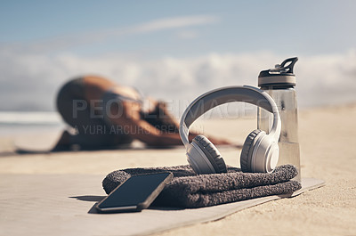 Buy stock photo Shot of a cellphone, headphones, towel and water bottle on the beach