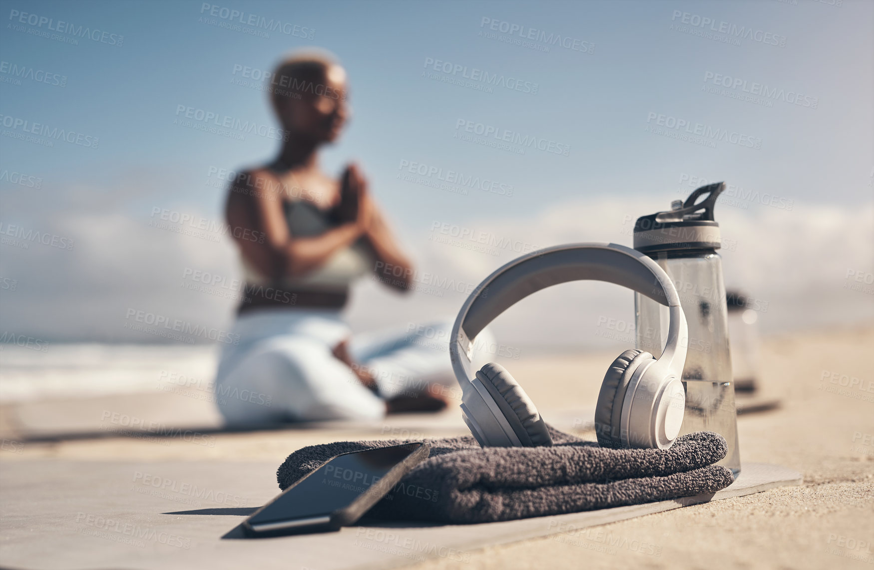 Buy stock photo Shot of a cellphone, headphones, towel and water bottle on the beach