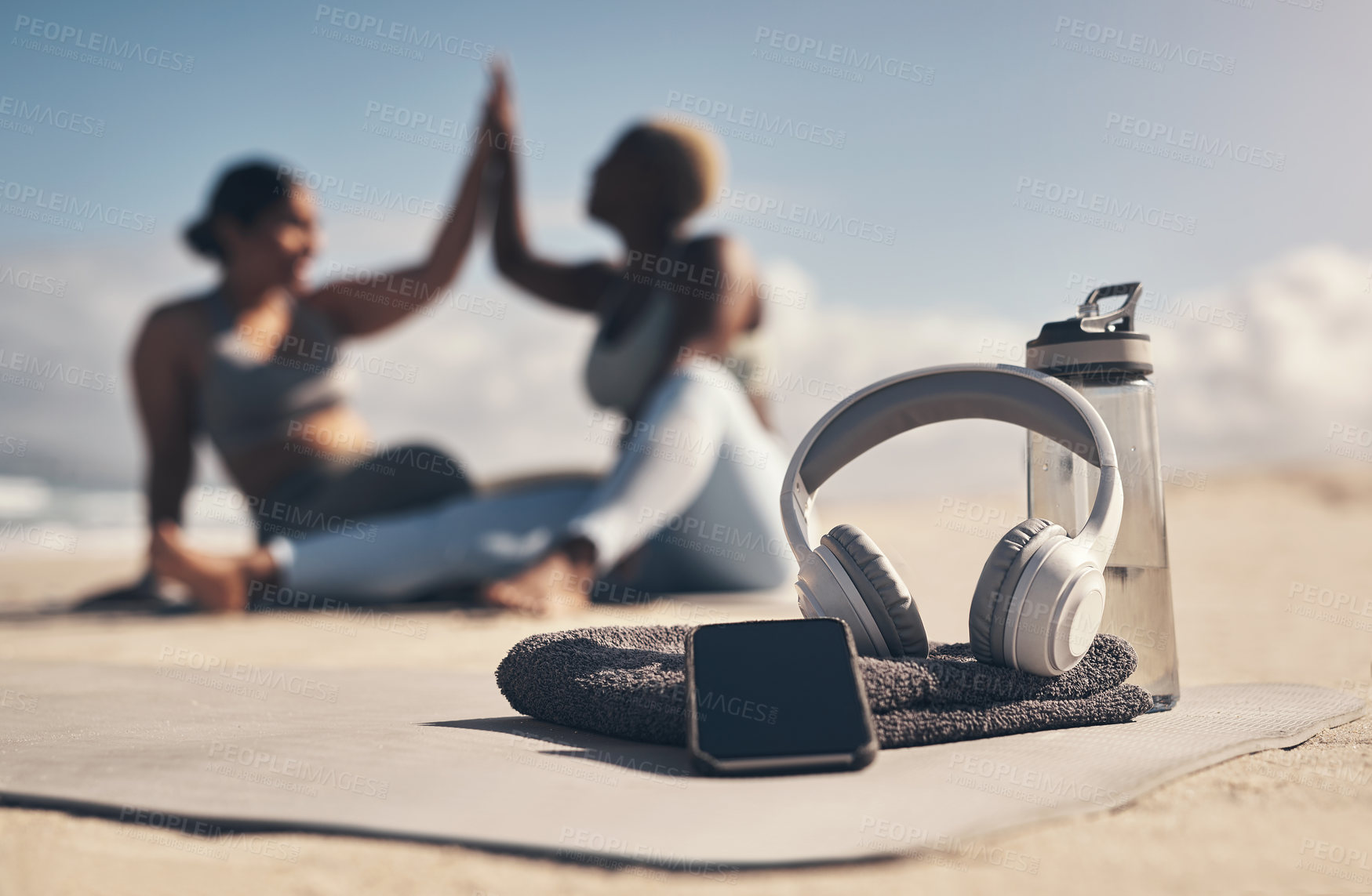 Buy stock photo Shot of a cellphone, headphones, towel and water bottle on the beach