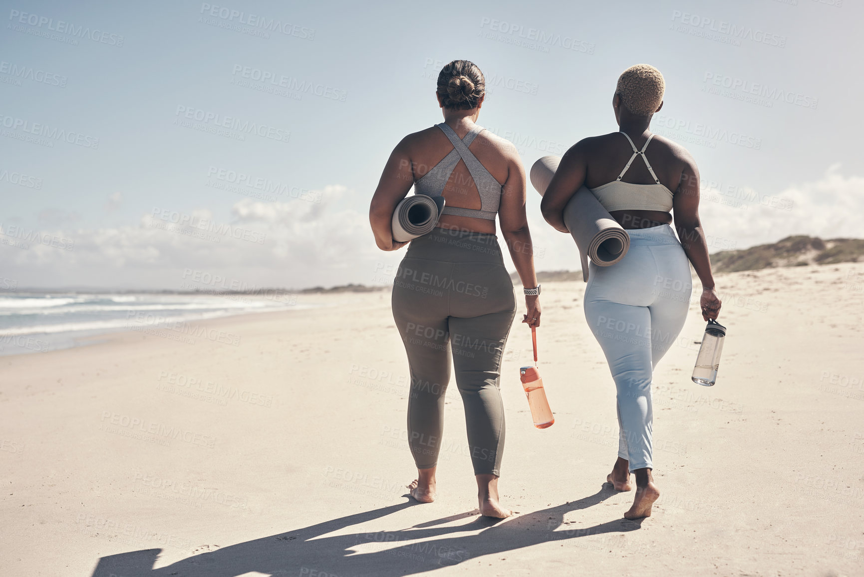 Buy stock photo Shot of two young women walking on the beach with their yoga mats