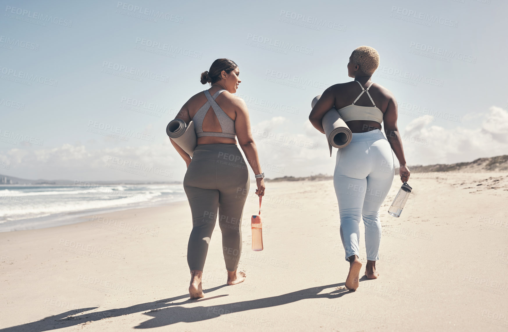 Buy stock photo Shot of two young women walking on the beach with their yoga mats