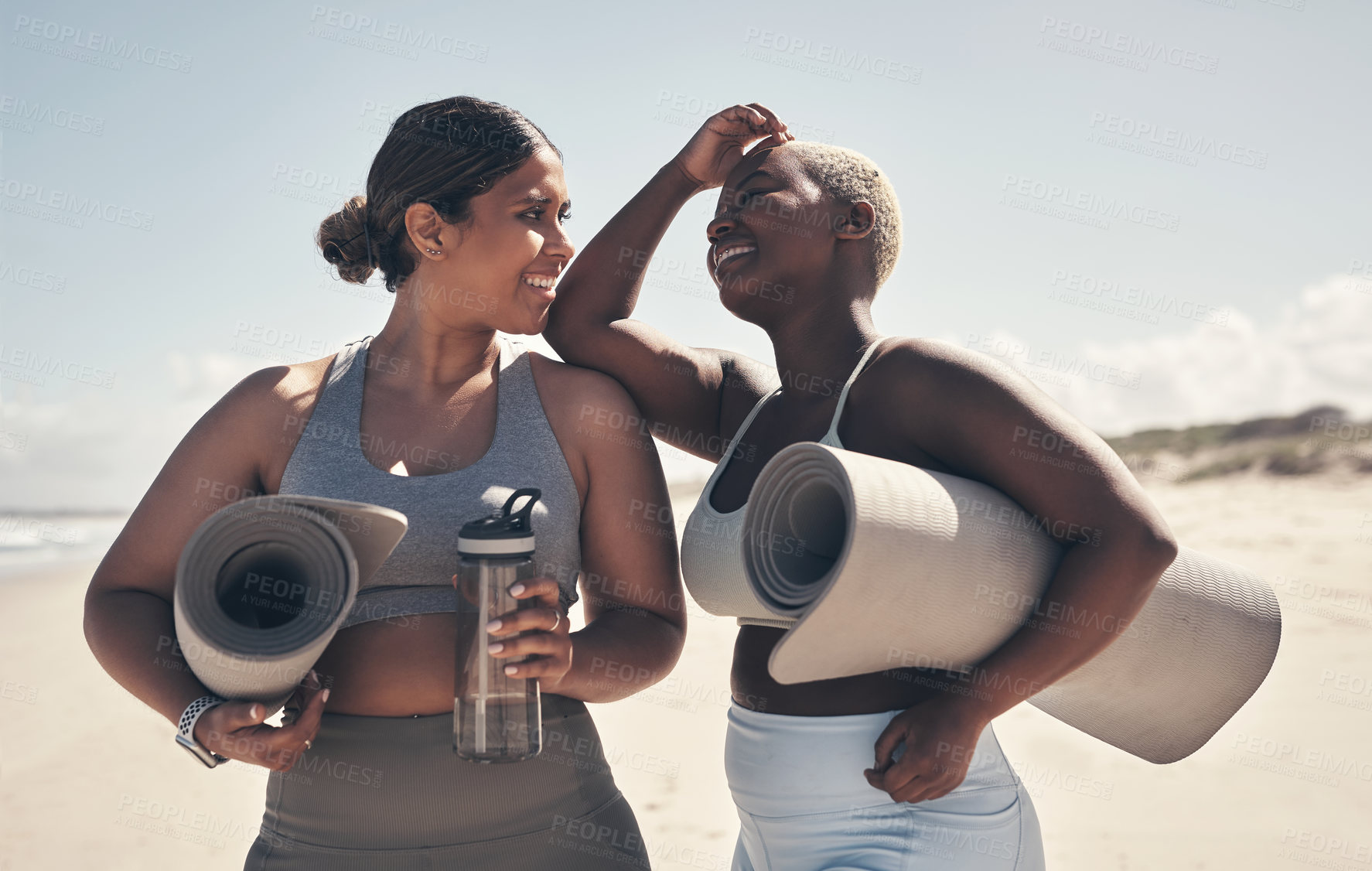 Buy stock photo Shot of two young women holding their yoga mats while  on the beach