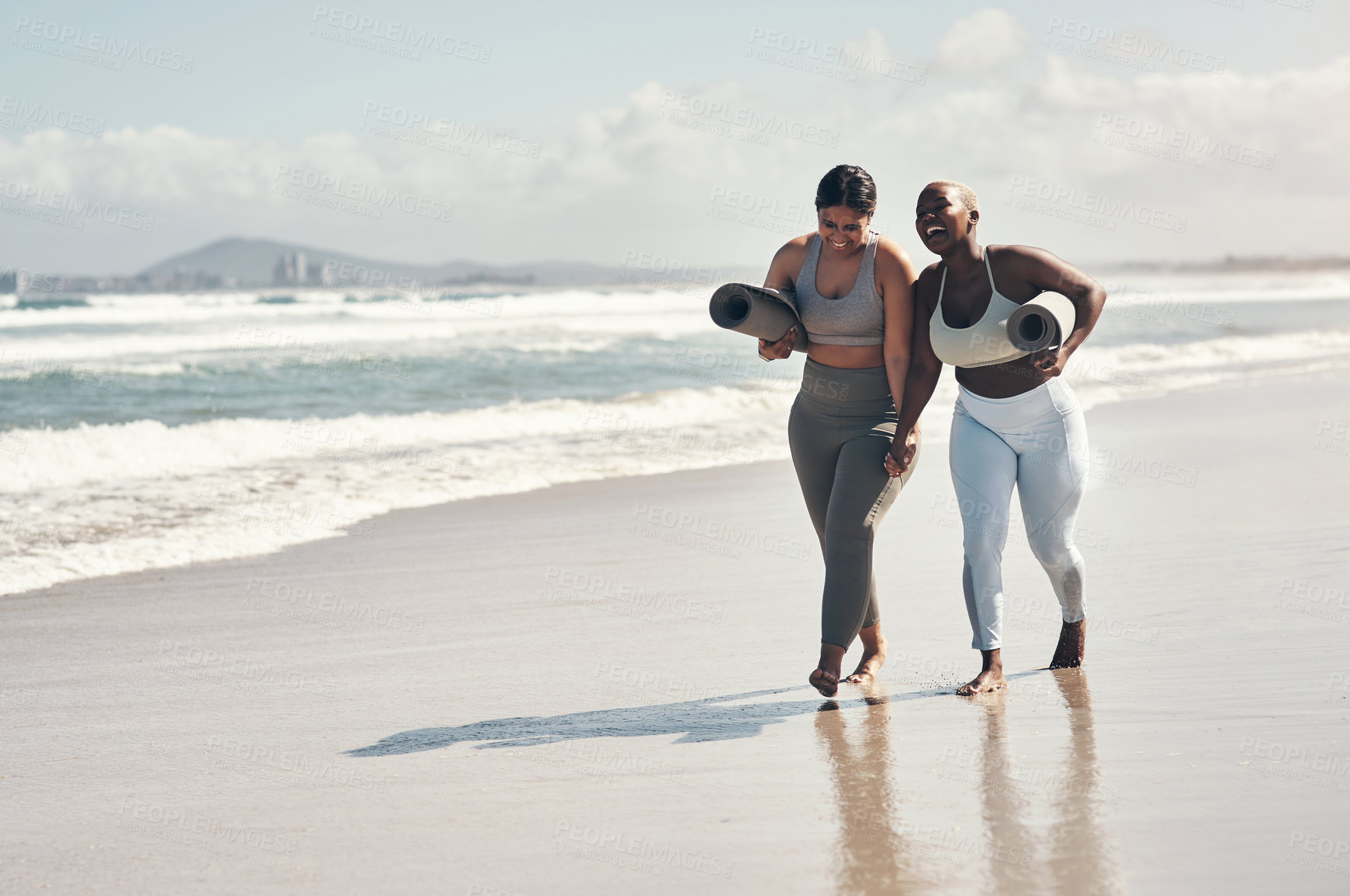 Buy stock photo Shot of two young women walking on the beach with their yoga mats