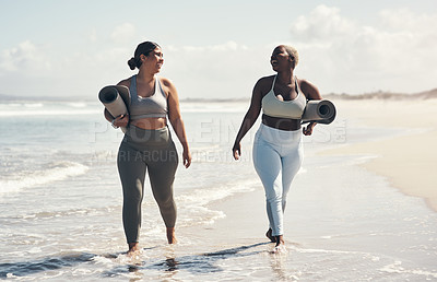 Buy stock photo Shot of two young women walking on the beach with their yoga mats