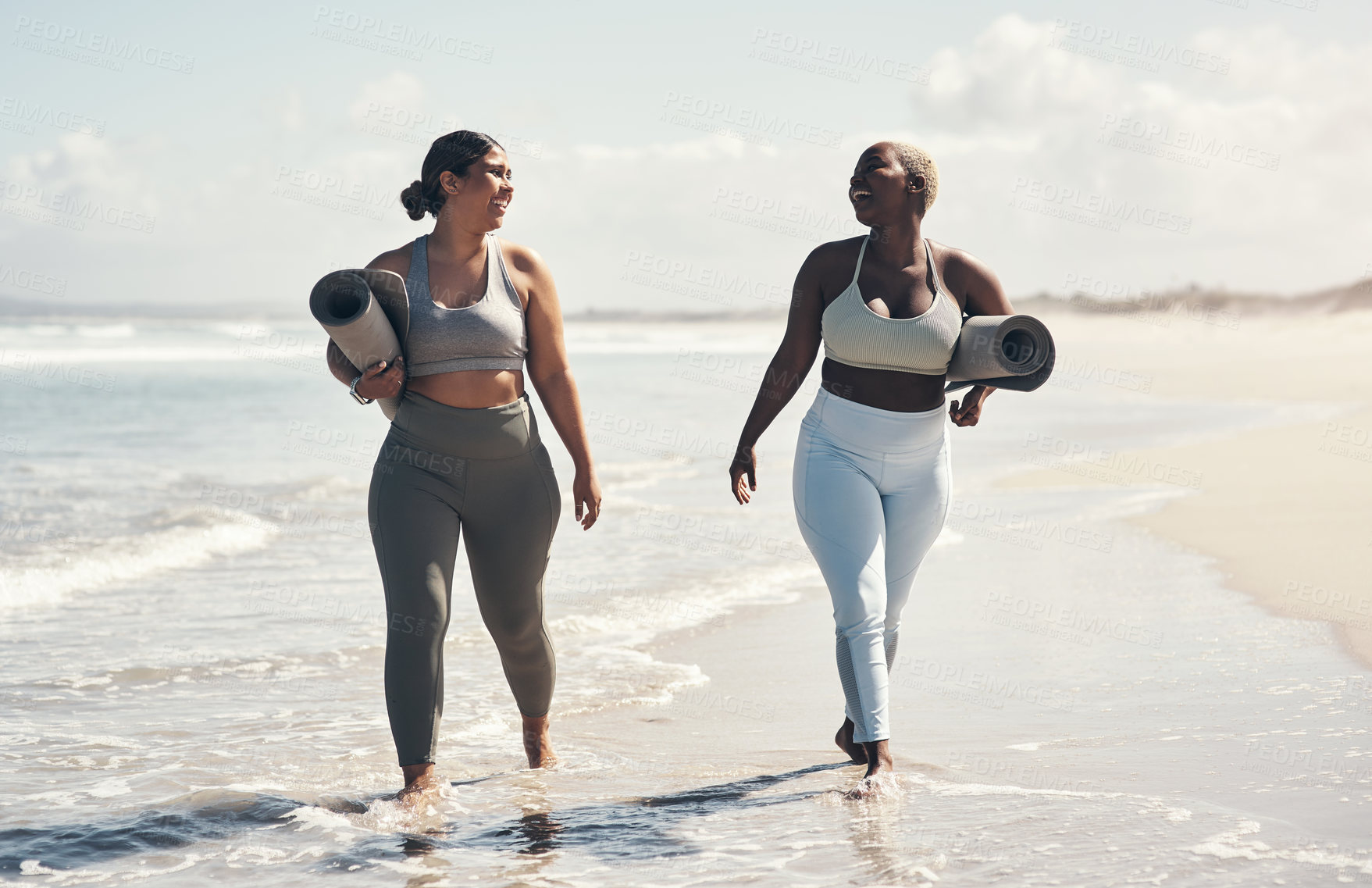 Buy stock photo Shot of two young women walking on the beach with their yoga mats