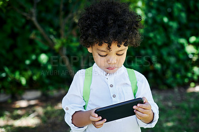Buy stock photo Shot of a little boy wearing a backpack while using a phone in nature