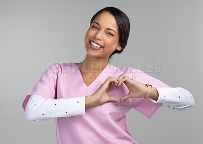 Buy stock photo Cropped portrait of an attractive young female healthcare worker gesturing a heart shape with her hands in studio against a grey background