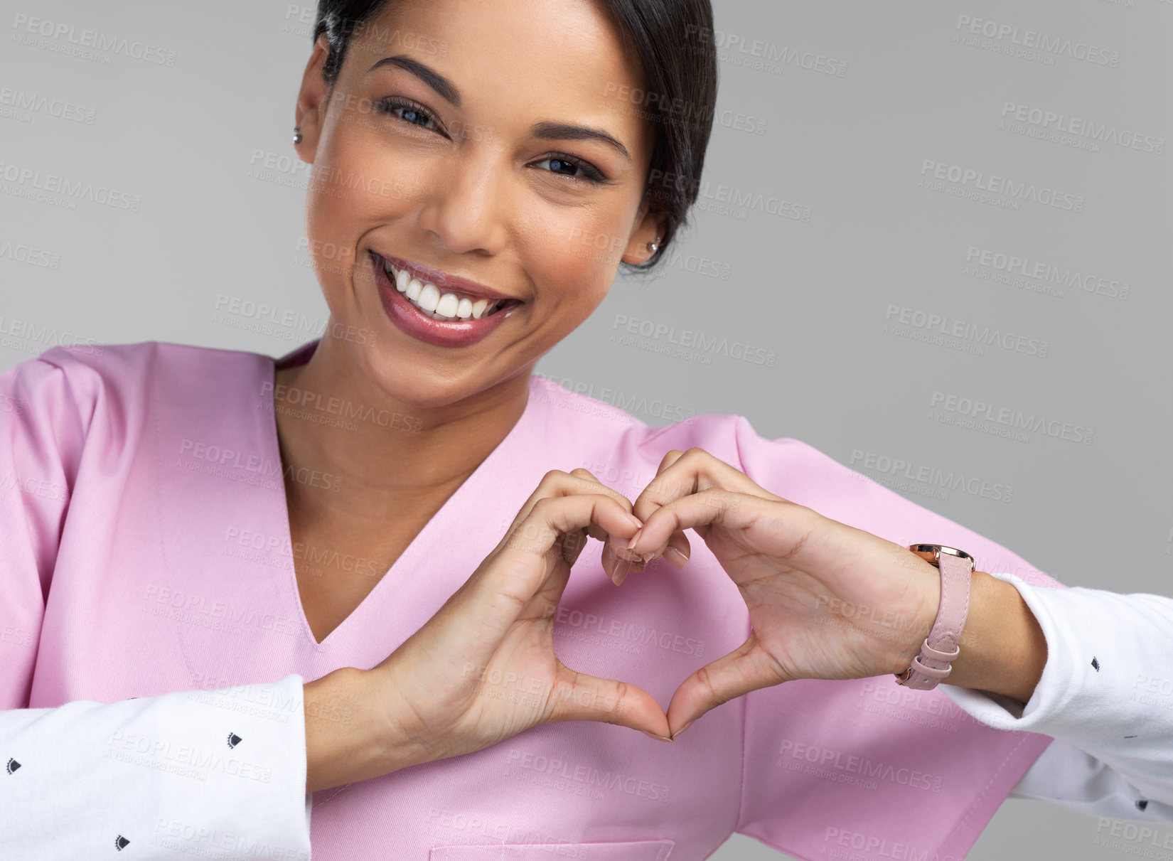 Buy stock photo Cropped portrait of an attractive young female healthcare worker gesturing a heart shape with her hands in studio against a grey background