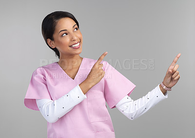 Buy stock photo Cropped shot of an attractive young female healthcare worker pointing towards copyspace in studio against a grey background