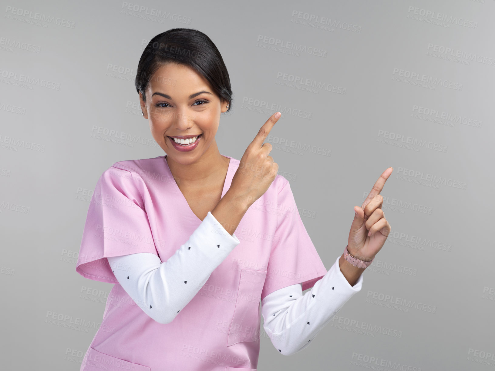 Buy stock photo Cropped portrait of an attractive young female healthcare worker pointing towards copyspace in studio against a grey background