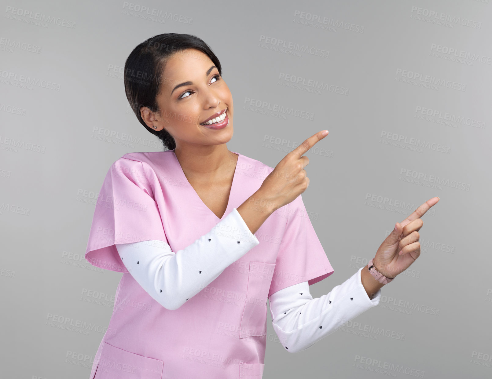 Buy stock photo Cropped shot of an attractive young female healthcare worker pointing towards copyspace in studio against a grey background