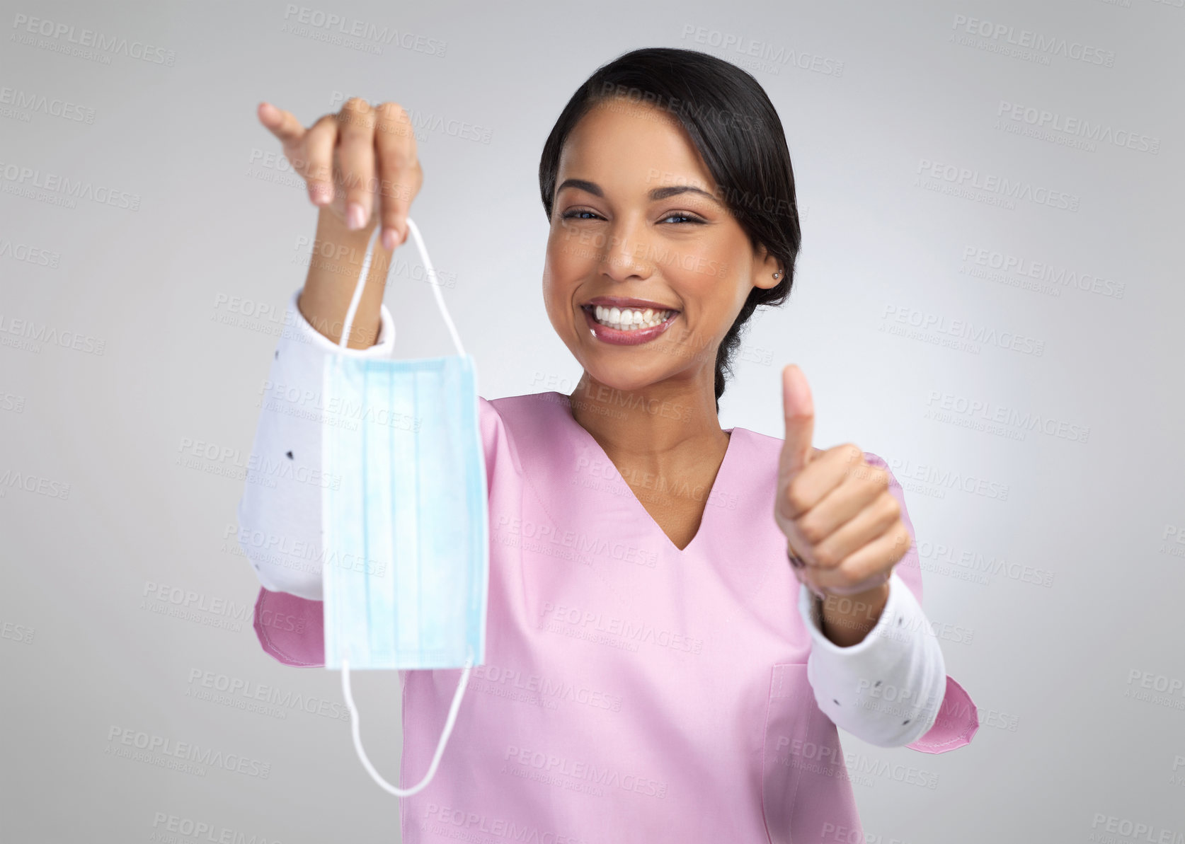 Buy stock photo Cropped portrait of an attractive young female healthcare worker holding up a mask and gesturing thumbs up in studio against a grey background