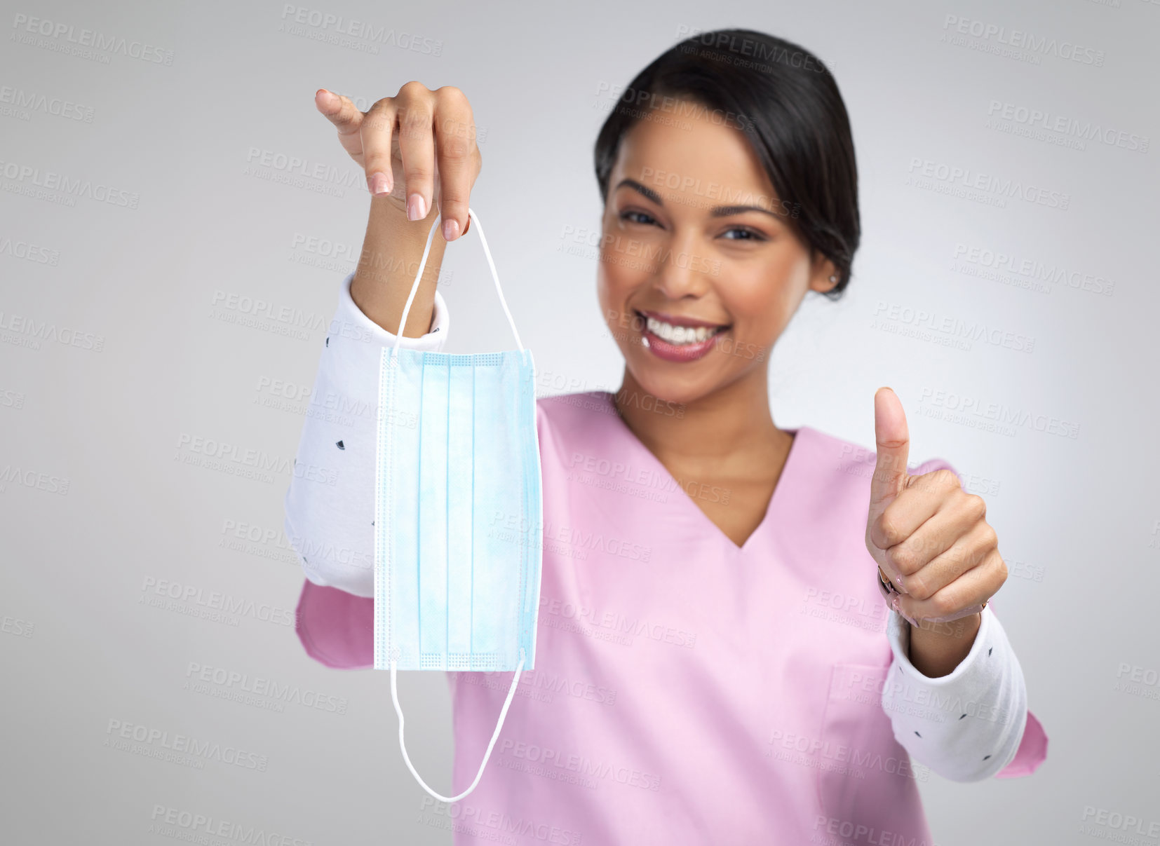 Buy stock photo Cropped portrait of an attractive young female healthcare worker holding up a mask and gesturing thumbs up in studio against a grey background