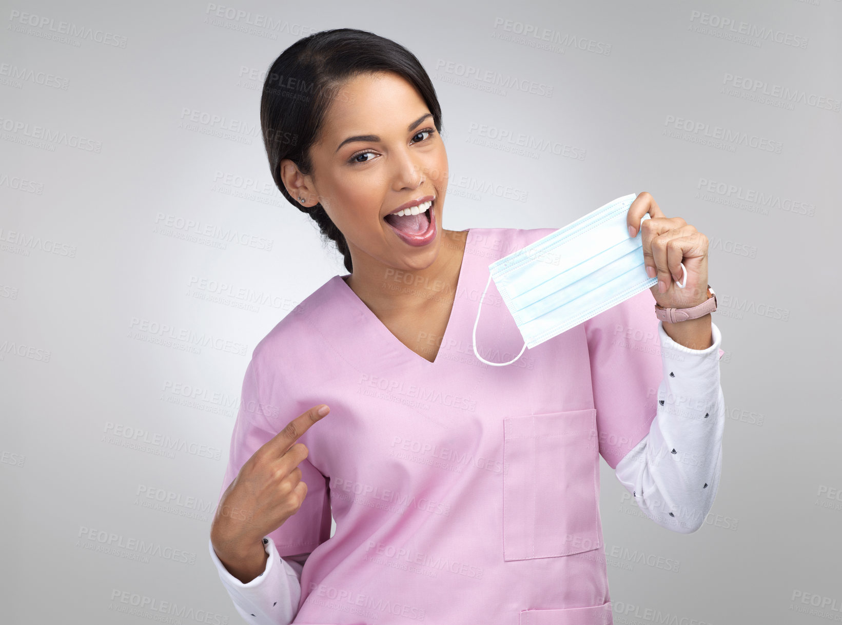 Buy stock photo Cropped portrait of an attractive young female healthcare worker holding up and pointing to a mask in studio against a grey background