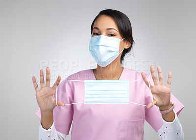 Buy stock photo Cropped portrait of an attractive young female healthcare worker holding up a mask in studio against a grey background