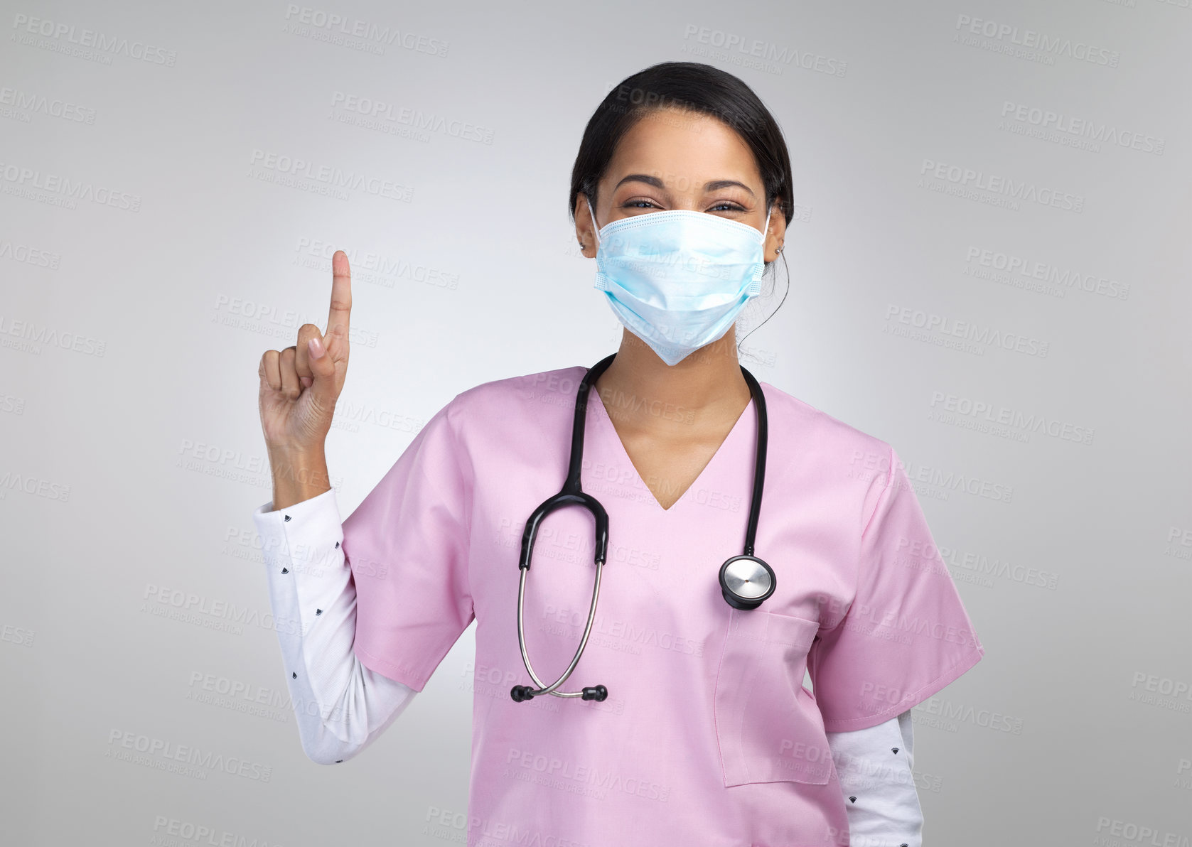 Buy stock photo Cropped portrait of an attractive young female healthcare worker wearing a mask and pointing towards copyspace in studio against a grey background