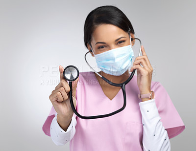 Buy stock photo Cropped portrait of an attractive young female healthcare worker wearing a mask and holding up a stethoscope in studio against a grey background