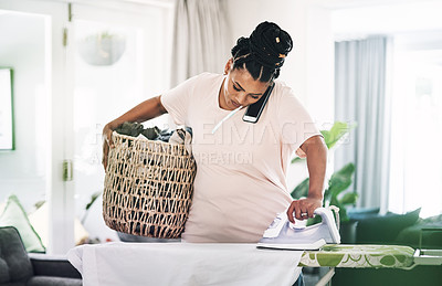 Buy stock photo Shot of a young woman ironing clothes while on the phone at home