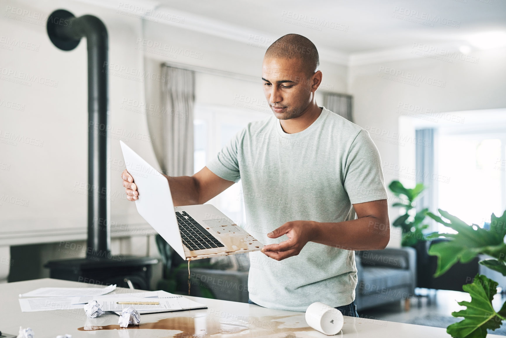 Buy stock photo Shot of a young businessman holding a laptop damaged by coffee at home