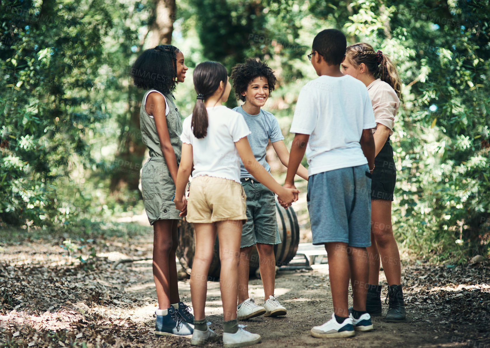 Buy stock photo Shot of a group of teenagers standing in a circle and holding hands in nature at summer camp