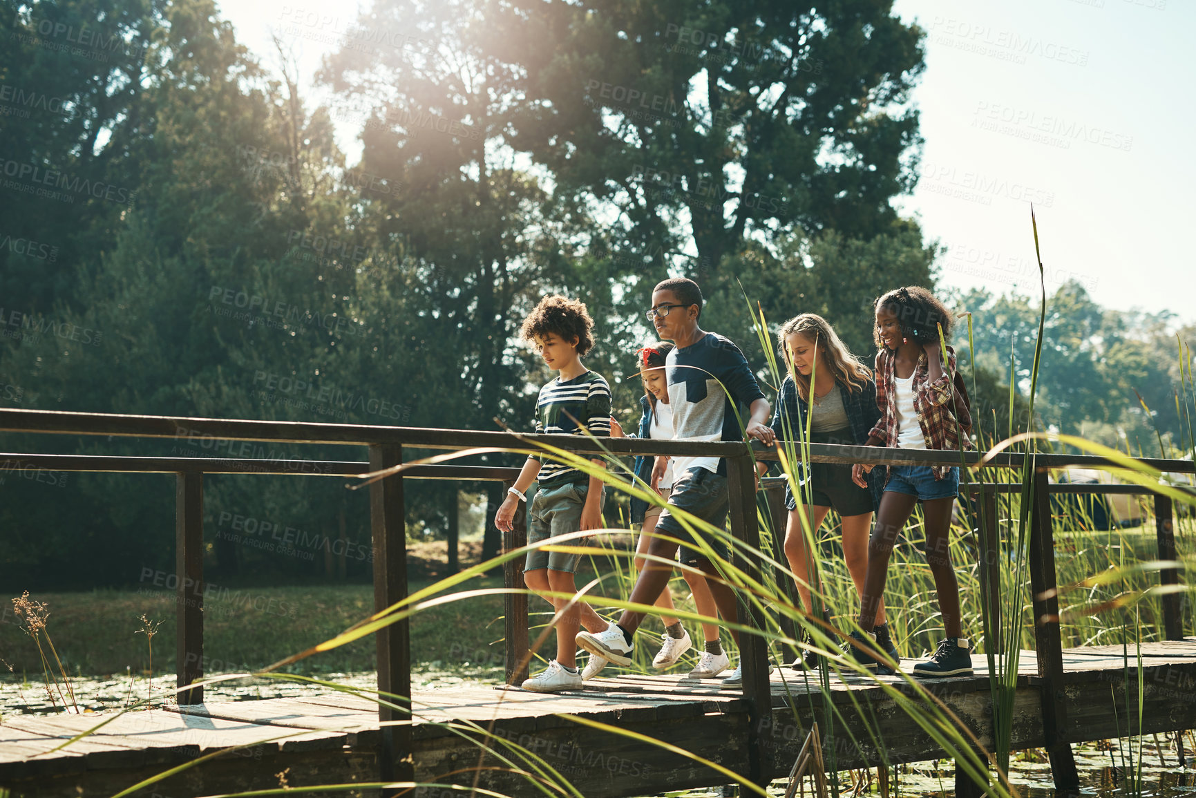 Buy stock photo Shot of a group of teenagers walking across a bridge in nature at summer camp