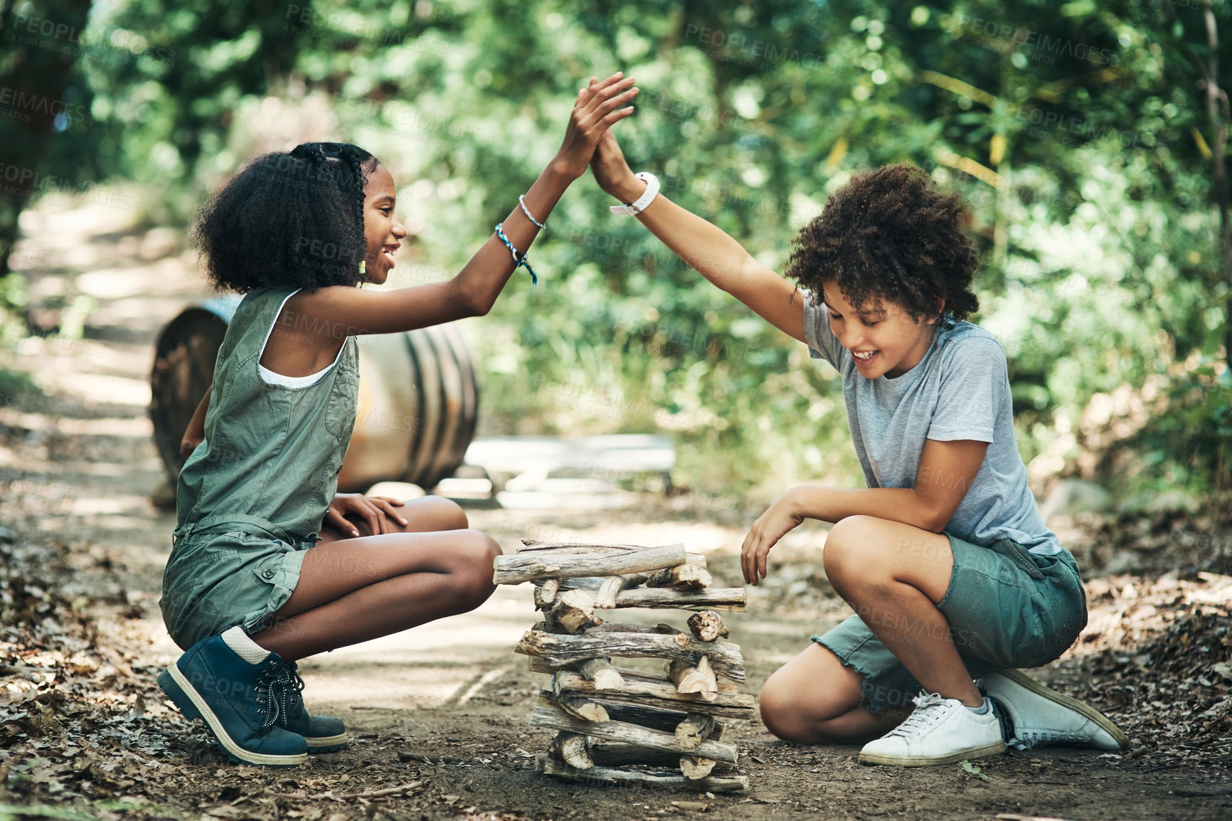 Buy stock photo Shot of a teenage boy and girl giving each other a high five while building a pile of wood at summer camp