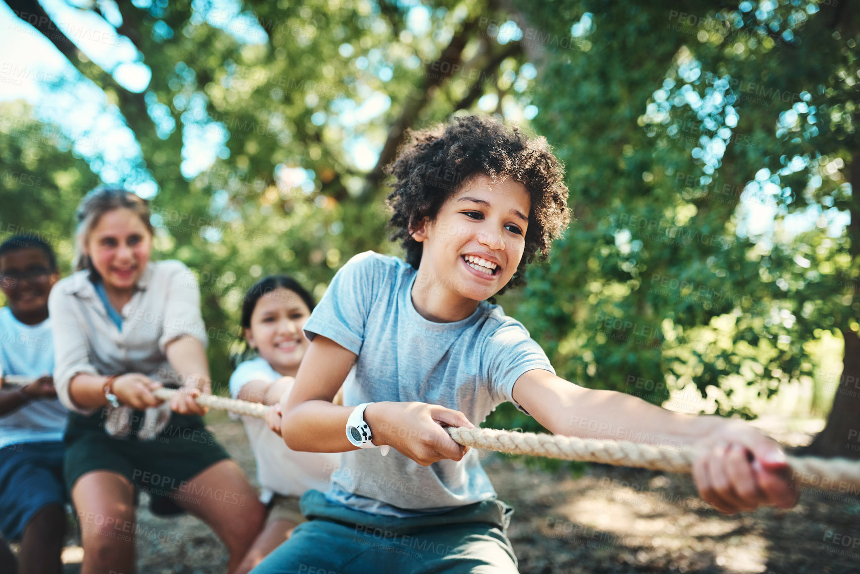 Buy stock photo Shot of a group of teenagers playing a game of tug of war at summer camp