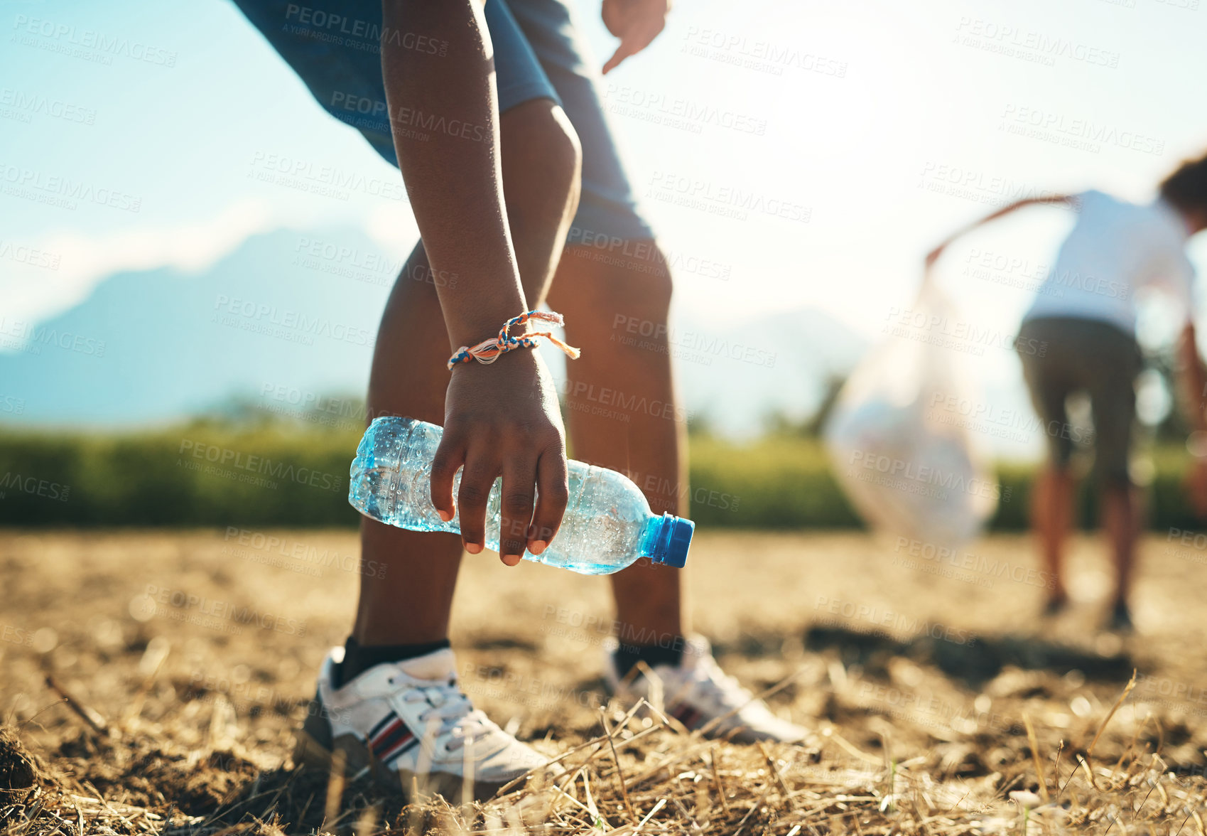 Buy stock photo Shot of an unrecognisable teenager picking up litter off a field at summer camp