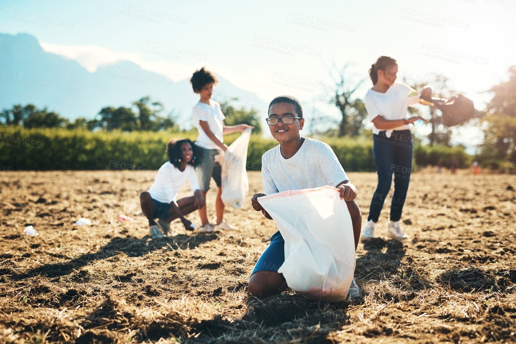 Buy stock photo Shot of a group of teenagers picking up litter off a field at summer camp