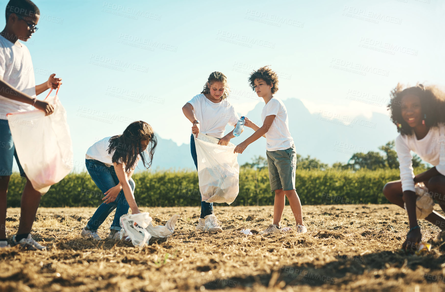 Buy stock photo Shot of a group of teenagers picking up litter off a field at summer camp