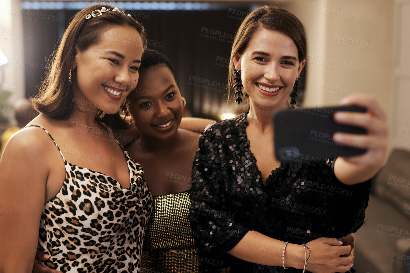 Buy stock photo Shot of a diverse group of friends standing together and using a cellphone to take selfies during a dinner party