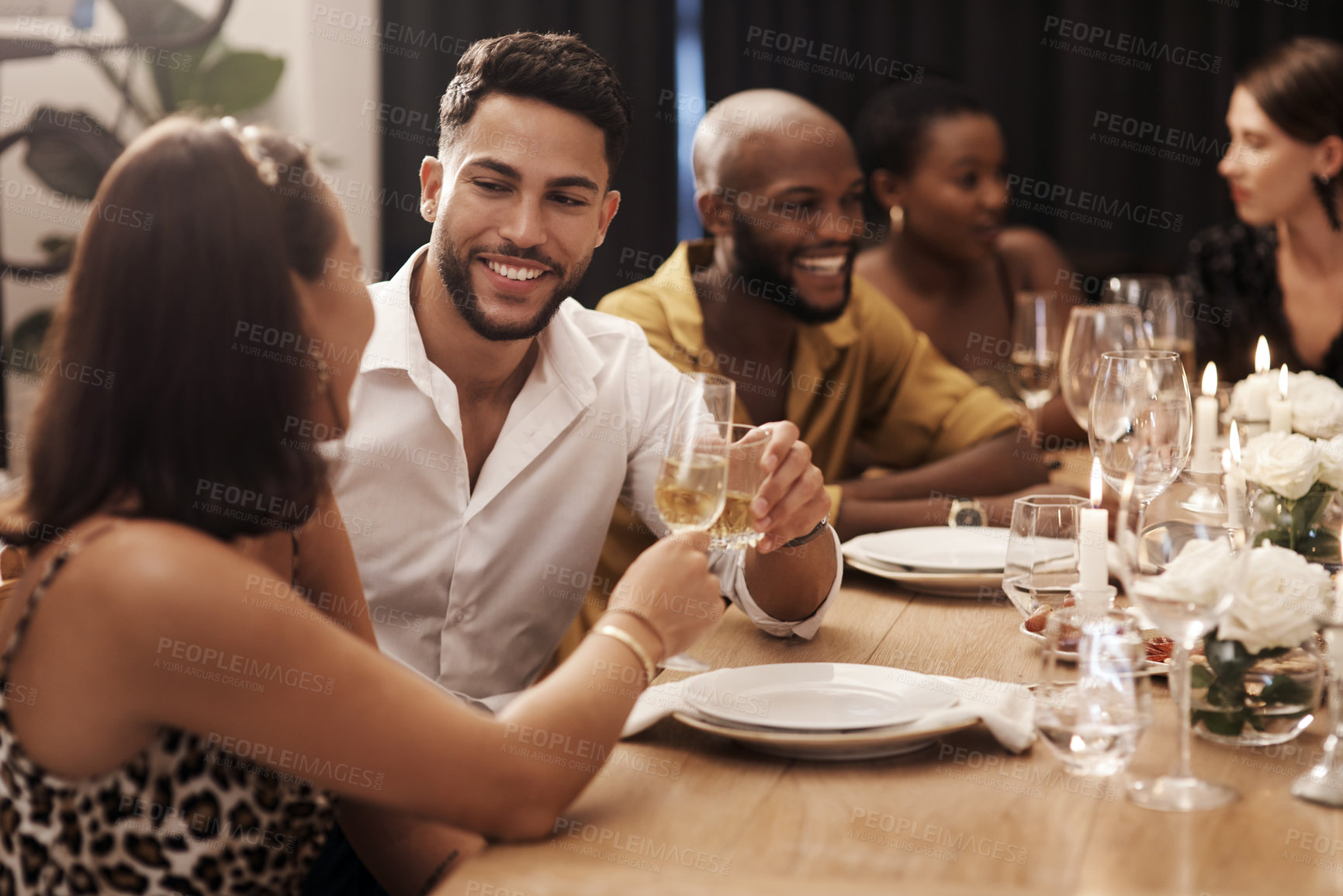 Buy stock photo Shot of a happy young couple sitting with friends and toasting with champagne during a New Year's dinner party