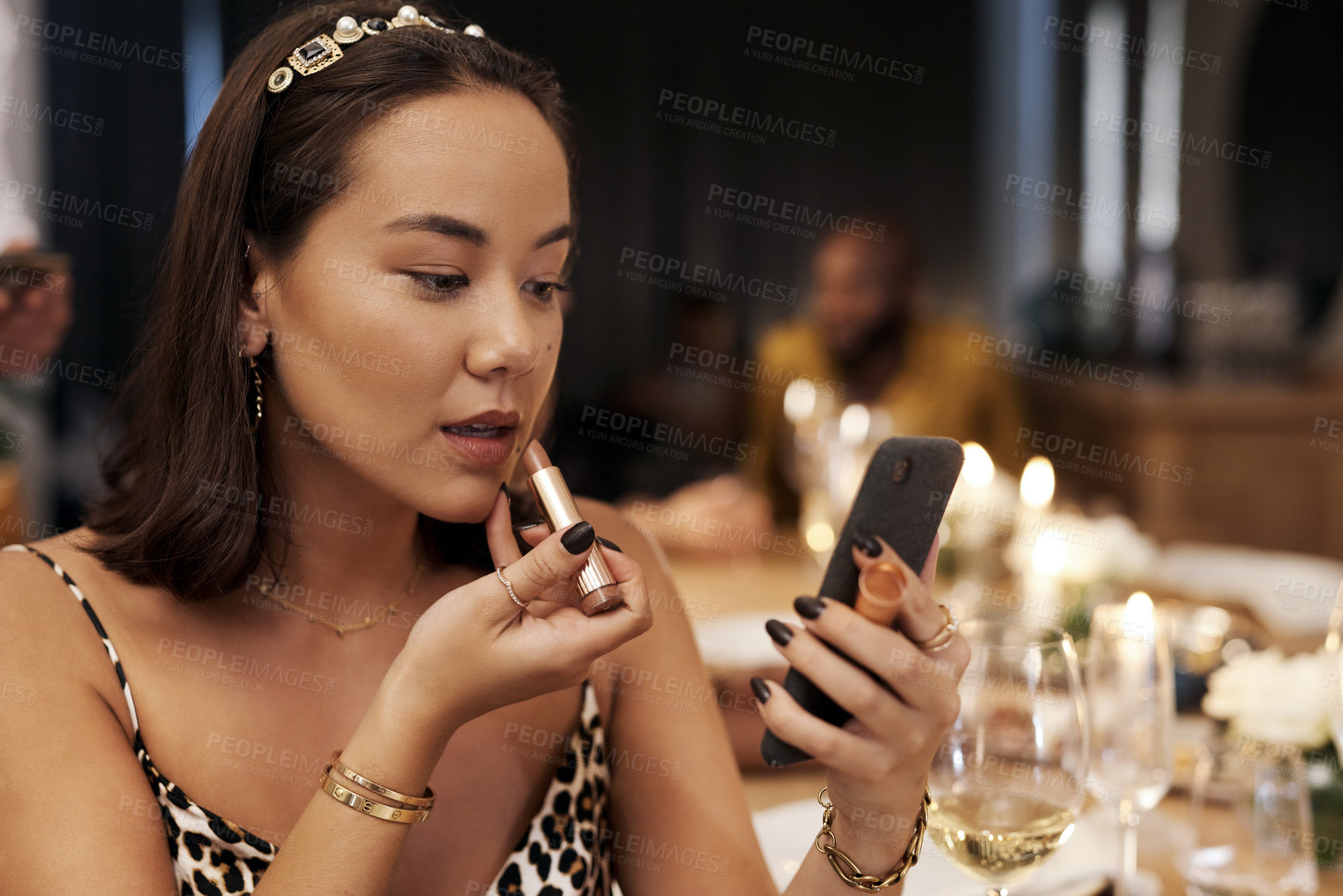 Buy stock photo Shot of an attractive young woman sitting alone and applying lipstick during a New Year's dinner party