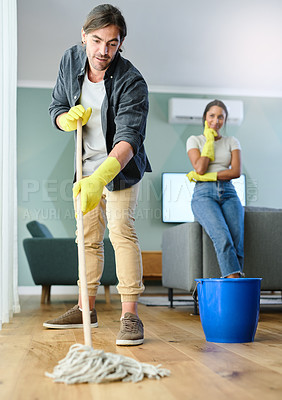 Buy stock photo Shot of a young man mopping the floor while his girlfriend watches him