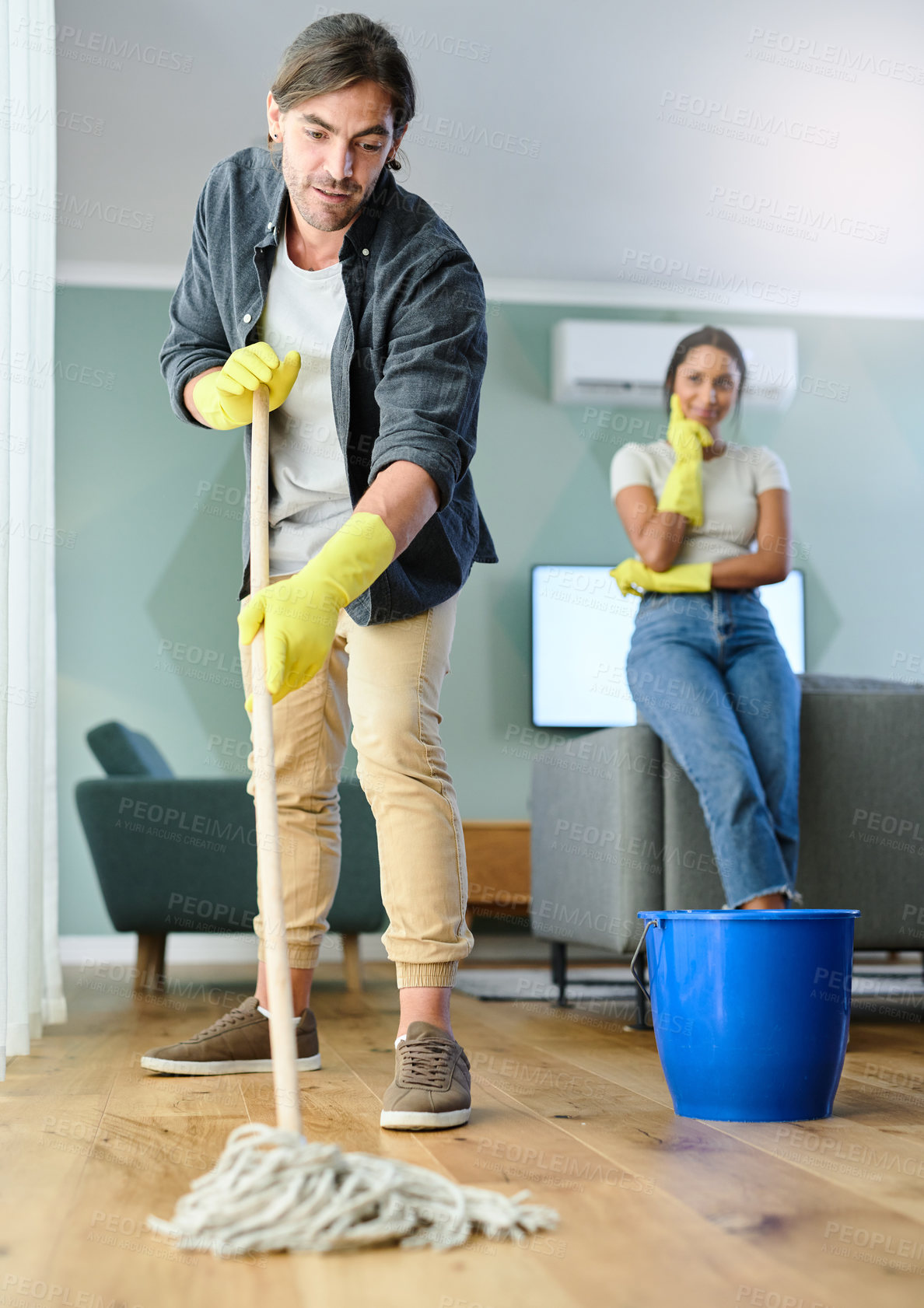 Buy stock photo Shot of a young man mopping the floor while his girlfriend watches him