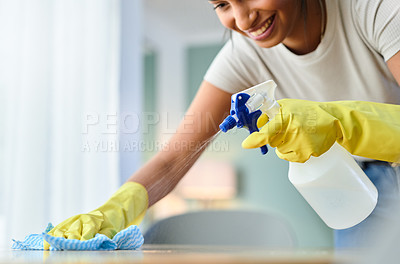Buy stock photo Shot of a young woman wiping a surface while spraying it with product at home