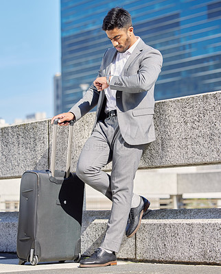 Buy stock photo Shot of a young businessman checking the time while standing with a suitcase in the city