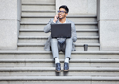 Buy stock photo Shot of a young businessman using a laptop while on the phone in the city