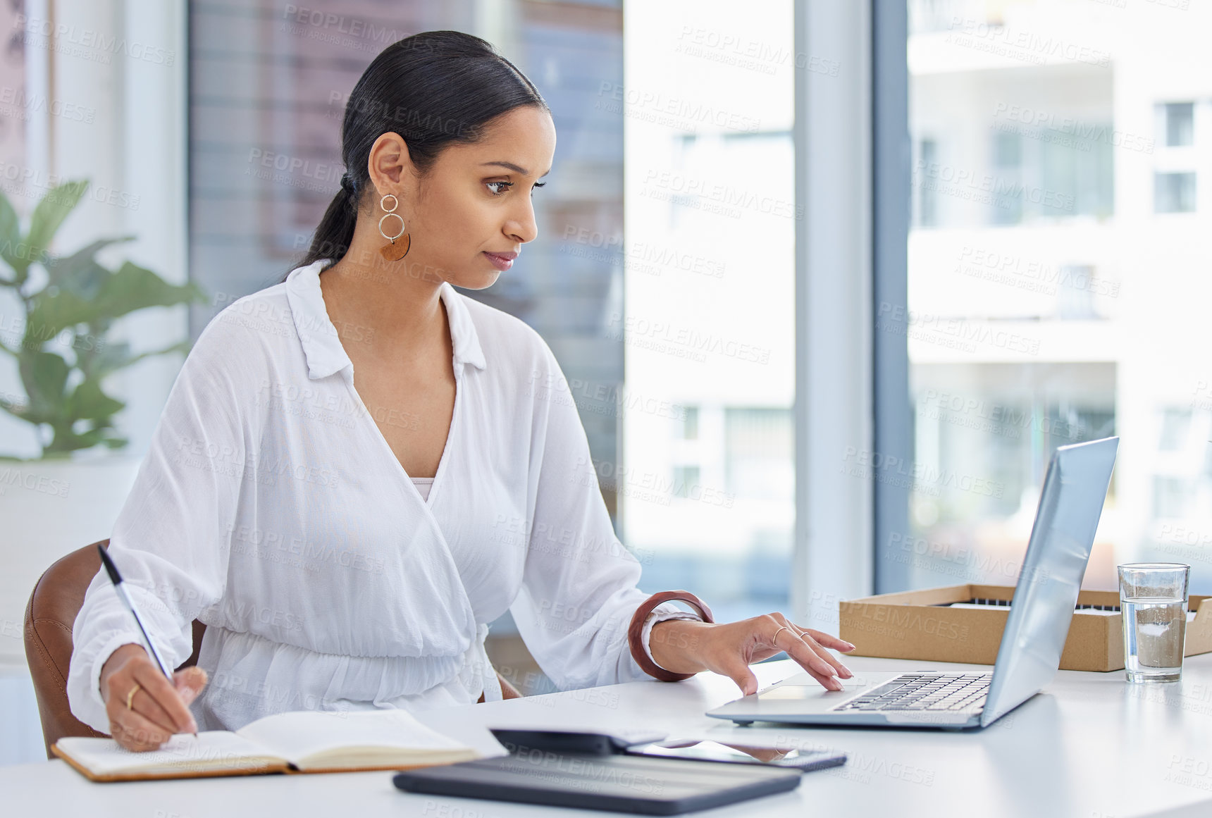 Buy stock photo Shot of a businesswoman using a laptop in a modern office and making notes in a notebook