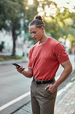 Buy stock photo Shot of a young man using his phone in the city