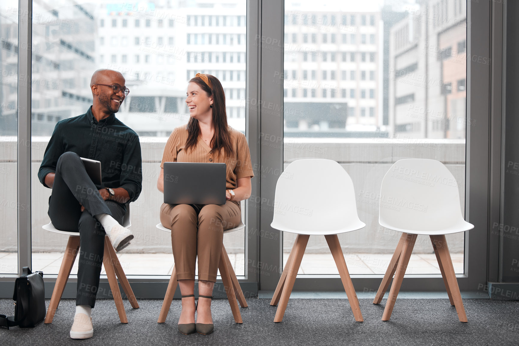 Buy stock photo Shot of two businesspeople sharing a laugh while using their electronic devices against a glass background in the city