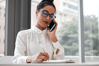 Buy stock photo Cropped shot of an attractive young businesswoman taking notes while making a phonecall at her desk in the office