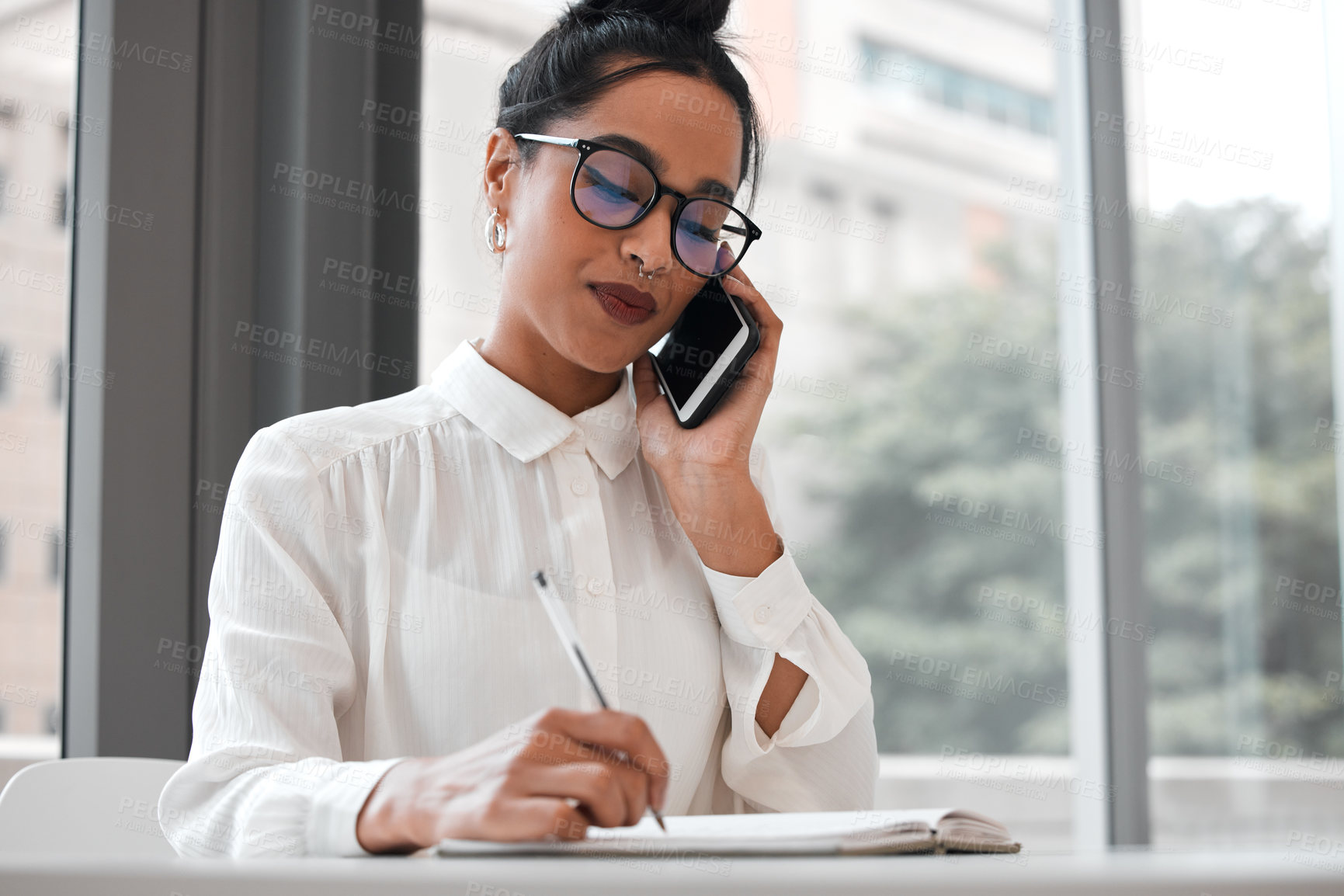 Buy stock photo Cropped shot of an attractive young businesswoman taking notes while making a phonecall at her desk in the office